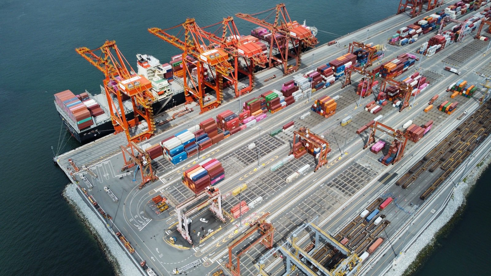 Container vessel beside cranes and organised cargo stacks at an international terminal